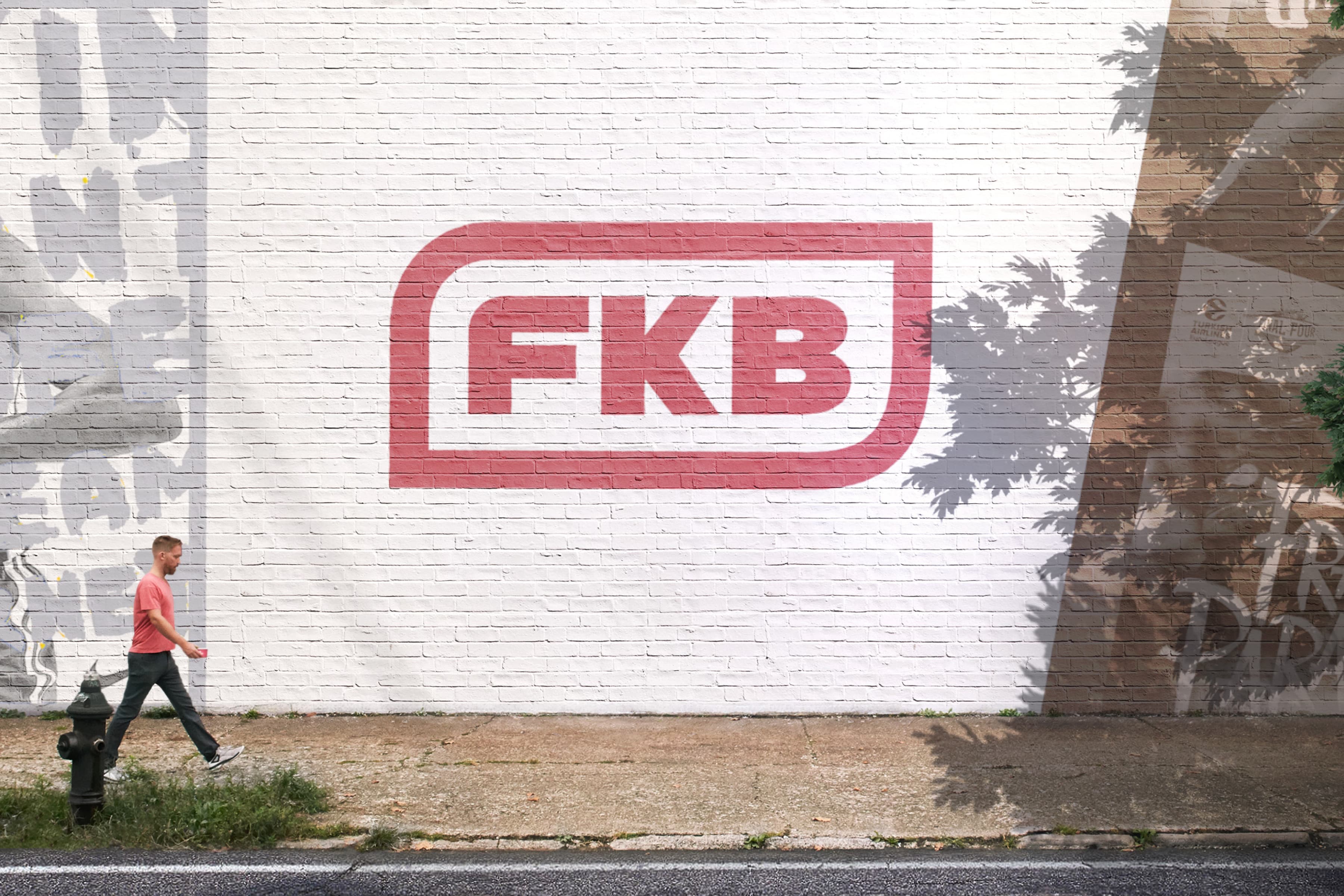 A man walking next to a white wall that features the FKB logo for FKB's Architecture website design.