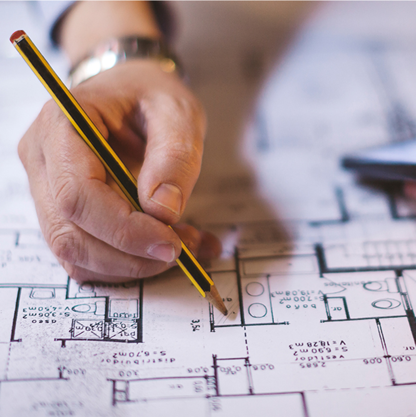 Hand of JJ White project manager finalizing drawing blueprints for building design and floor plan.