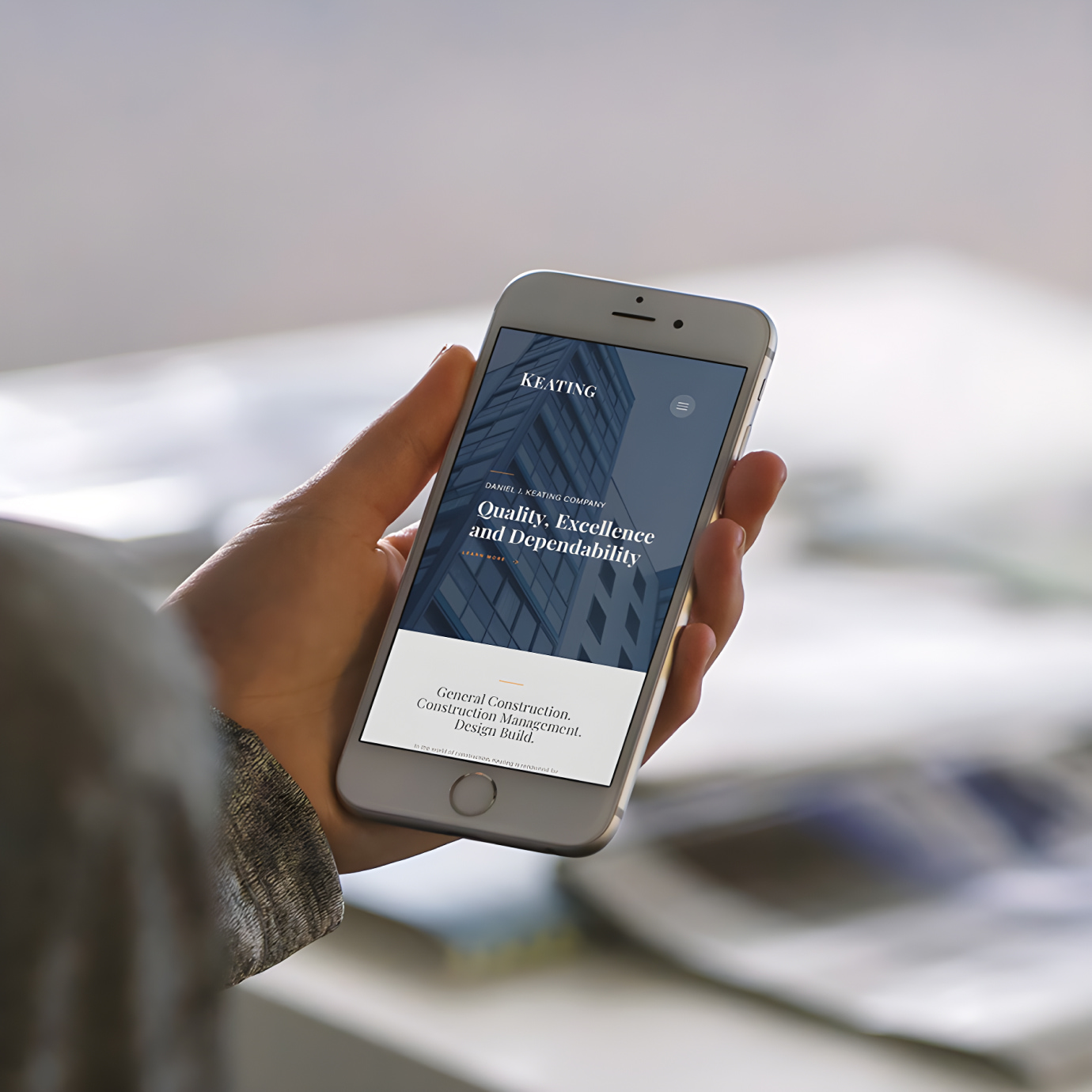 Hand holding smartphone with a mockup of Keating construction website design page on screen.