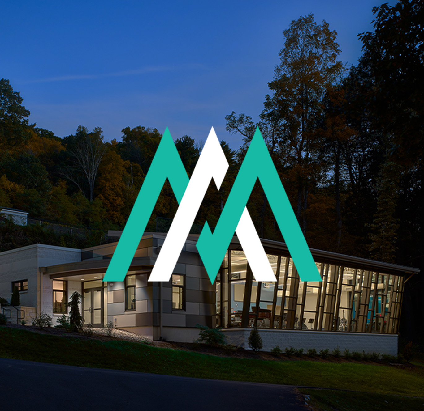 Modern building with large windows at dusk, overlaid with the stylized logo of Millan for their Architecture website design.