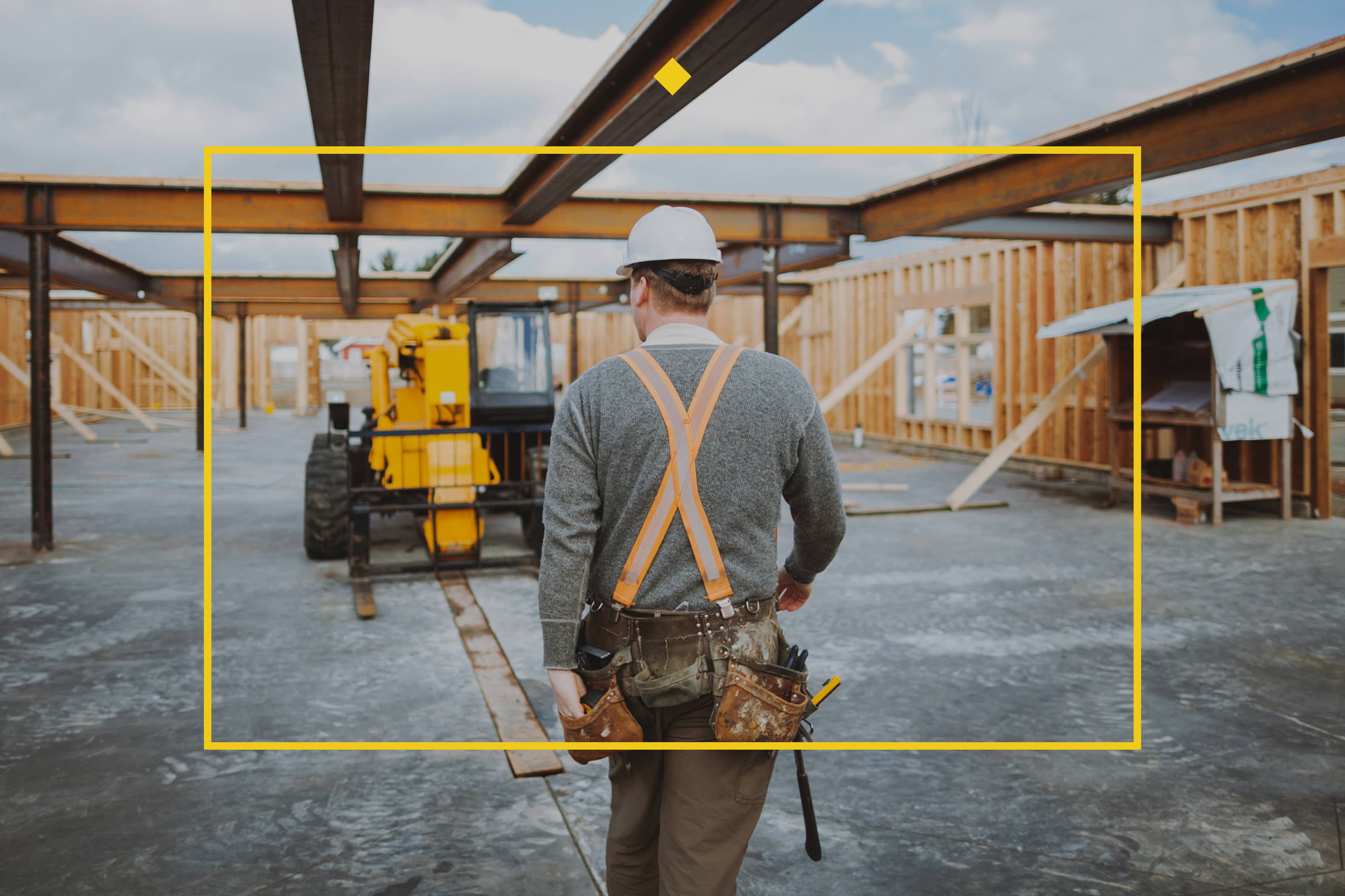 JJ White branded project manager walking towards a forklift with a yellow frame in the foreground for construction website design page.